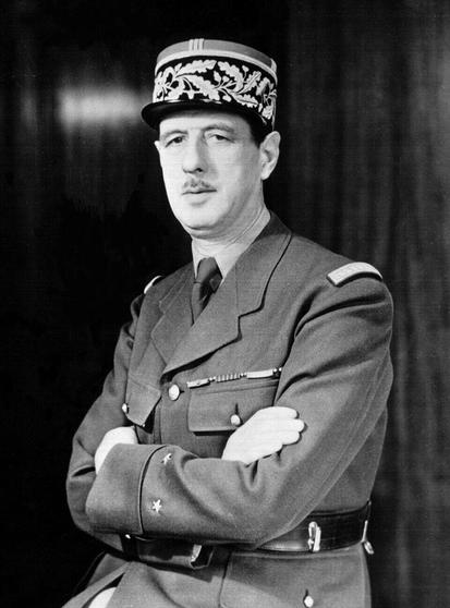 Photographie en noir et blanc de Charles de Gaulle en 1942, durant la Seconde Guerre mondiale, portant un uniforme militaire français et un képi. Il se tient de face, les bras croisés sur la poitrine, affichant une expression sérieuse.
