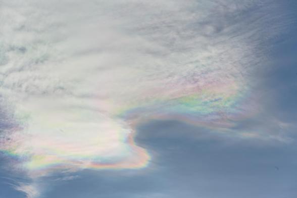 Dünne Wolken von einem blassnblauen Himmel. Der Rand der Wolken schimmert in Perlmuttfarben.