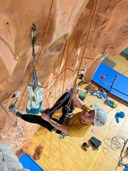 Personne en train de remonter une corde fixe sur un mur d'escalade artificiel