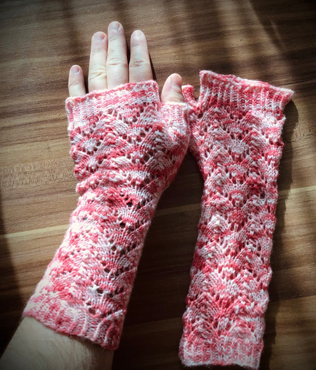 I show off a pair of knitted fingerless gloves made from white yarn speckled with red dye