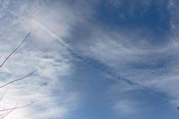 Blick auf eine dünne Wolkenschicht, darin ein Strich, wo die Wolken verschwunden sind. Daneben geht diese Lücke in einen Kondensstreifen über.