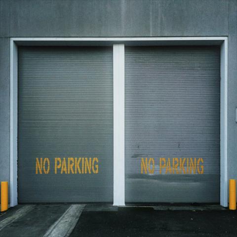 Two very tall, gray, industrial garage doors remain closed, with yellow text painted on the front that reads, "NO PARKING."