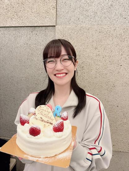 A woman wearing glass smiling holding a birthday cake.