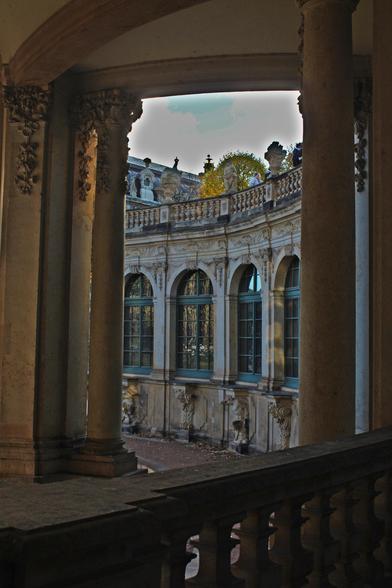 A baroque castle made of bright stone with blue window frames photographed from out of  stone hallway.