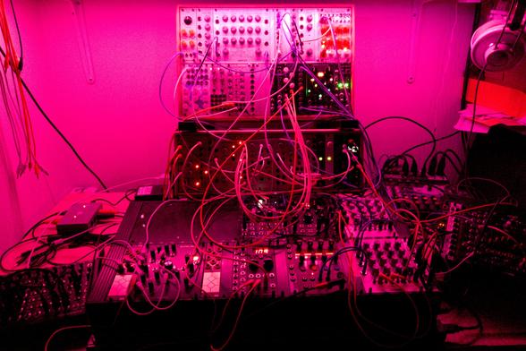A patched Eurorack synthesizer bathed in magenta light, ready for playing.