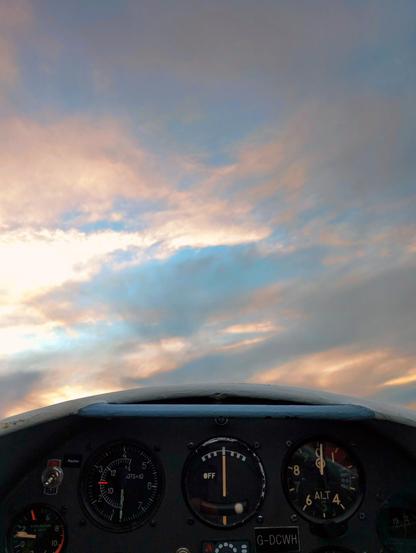 A glider cockpit set against a cloudy evening sky, with scuds of gold running through