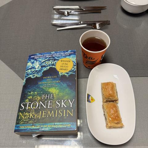 The book "The Stone Sky" by N. K. Jemisin lying next to a plate with baklava and Turkish tea
