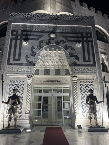 Epic entrance of a white building with blue ornaments. Two statues with spears are standing on each side of the entrance like soldiers.