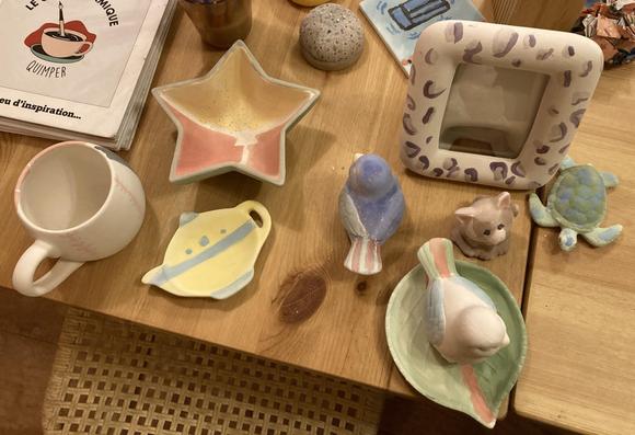 Plusieurs objets en céramique posés sur une table en bois : une tasse blanche, des oiseaux de différentes couleurs, un cadre, une tortue verte