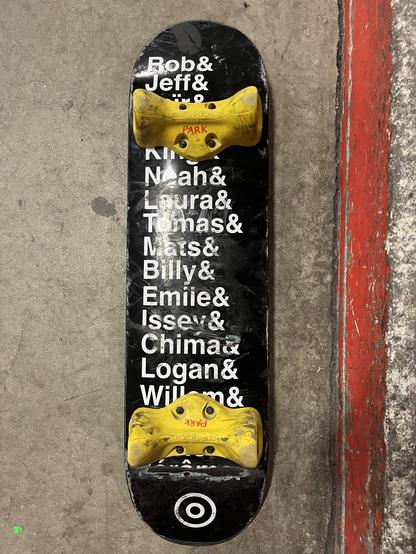 Skateboard with bold Helvetica white on black with a list of about 16 names ending with an ampersand