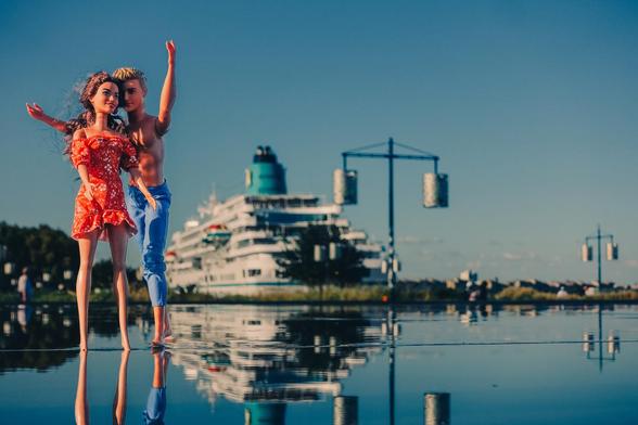 Two dolls on water with a giant (real) cruise boat in the back.