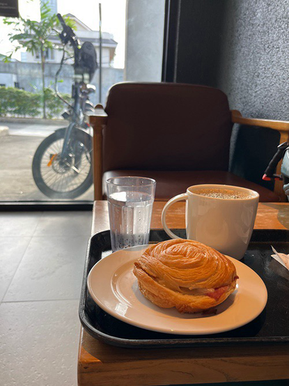 Photo of a tray of food on a table at a cafe and in the background is a bicycle parked outside next to the glass door