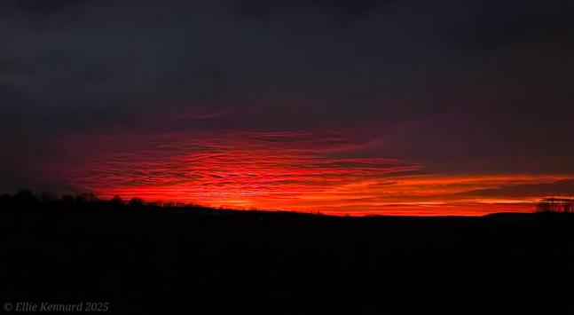 A very dark foreground is under a flame red sky with horizontal streaks of dark clouds through the red.