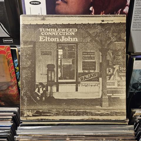 Album cover features an old timey, brown patina photo of EJ sitting in front of what is supposed to look like an old American train station. It was actually taken at Sheffield Park station in Essex, UK.