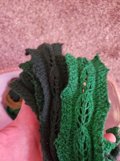 A handful of knitted lace bookmarks with a repeating leaf motif. They are various shades of green.