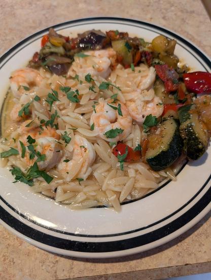 A plate with shrimp scampi over orzo pasta with grilled summer veggies