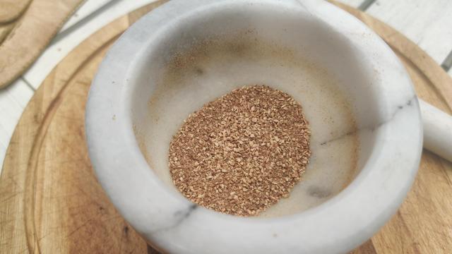 A mortar and pestle with some ground Moreton Bay fig seeds in it. They look brown and gritty.