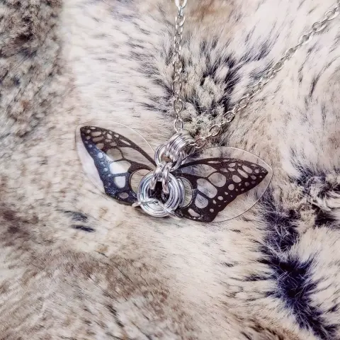 Autre pendentif de papillon, plus petit, utilisant seulement deux écailles à fond transparents. Le motif est noir.