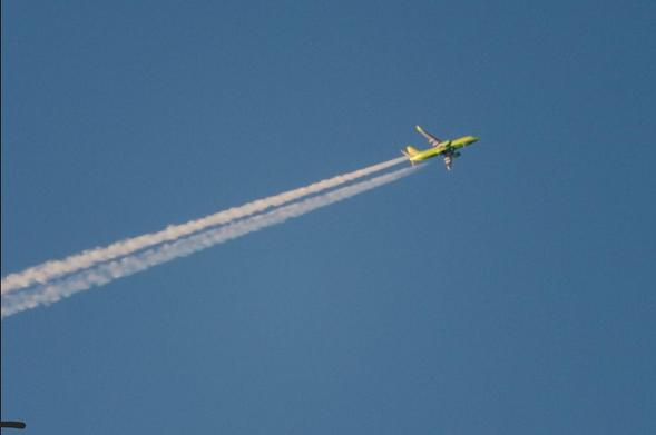 Ein hochfliegendes, grünes Passagierflugzeug mit Kondensstreifen vor blauem Himmel.