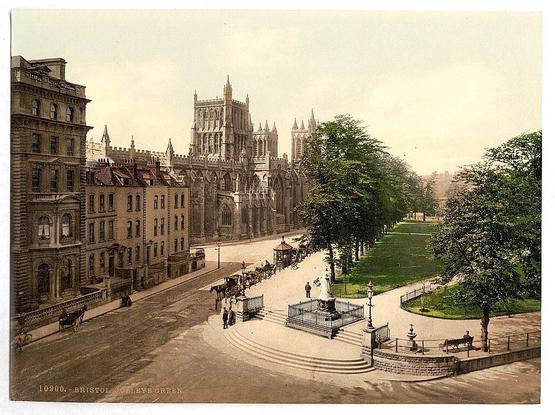 This historical image depicts a bustling urban scene from around 1890 to 1900. In the foreground, there's an expansive street with numerous pedestrians and horse-drawn carriages traversing it. A notable architectural structure is prominently displayed in the background - what appears to be a cathedral or significant church building with intricate Gothic architecture featuring pointed arches, tall spires, and large windows. The surrounding buildings have ornate detailing typical of European urban development during this period.

The green space on both sides adds a serene touch against the bustling street scene, suggesting that College Green in Bristol was not only an area for commerce but also a place meant for relaxation or social gatherings. This print is indicative of photographic techniques prevalent at the time and provides insight into daily life and architectural styles of early 20th-century Britain.

This image captures both everyday urban activity and historical architecture, offering valuable visual information about late Victorian-era England's societal structure and aesthetic preferences.