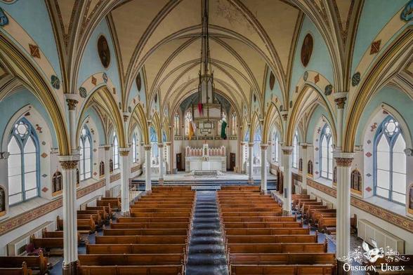 The photo shows a breathtaking view inside an abandoned church. Pews stretch toward the altar under arched ceilings with intricate designs