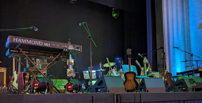 A stage in The Regal, setup for a performance from the group Lindisfarne.
A Hammond organ on the left and a range of guitars and drum kit fill the rest of the stage, illuminated with blue/green lighting