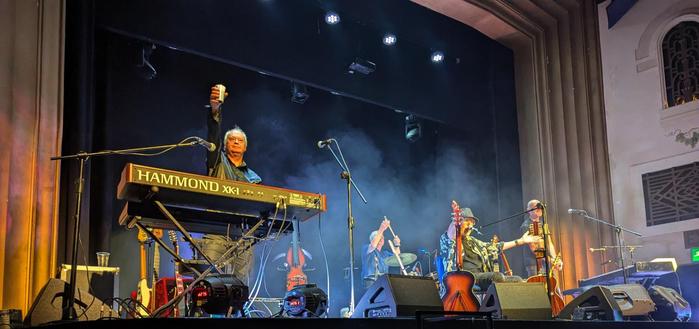 At the end of the show, the group on stage reacting to the applause of the crowd after a fantastic show. The stage background contains quite a bit of theatrical 'smoke' illuminated by white light (The last song being appropriately 'Clear white light')