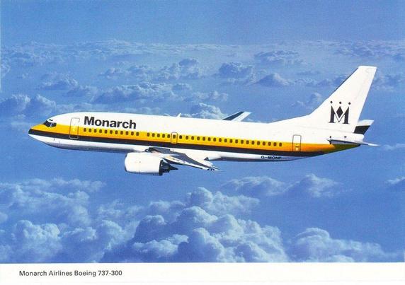 A Monarch Airlines Boeing 737-300 is captured in mid-flight above a sea of soft, layered clouds. The aircraft is painted in the airline’s classic 1980s–1990s livery: a clean white fuselage with a bold yellow stripe bordered by orange, running the length of the plane. The word “Monarch” appears prominently near the front, while the tail features the stylized black “M” crowned with three dots. The jet is angled slightly upward, suggesting a smooth climb through bright blue skies. Sunlight washes over the aircraft, emphasizing its sleek lines, and engines. The image conveys a calm, confident sense of travel and the distinctive identity of the now-historic British airline.