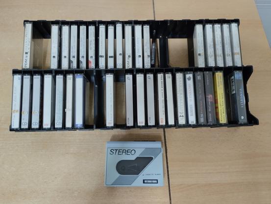 Foto de um arquivador com arredor de trinta cassetes, a maioria em fitas regraváveis.

Abaixo, um walkman cor azul claro.