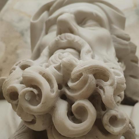 Fragment of a white marble sculpture with a highly detailed, stylized beard of the figure, which consists of large, deeply carved, spiral, and curl-like locks.