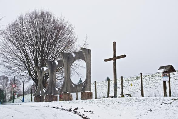 U vodojemu - strom, betonové skulptury s velkými kulatými otvory, kříž a informační cedule.