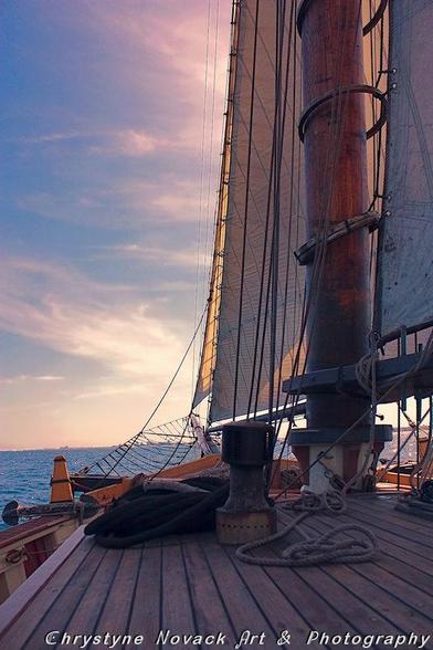 A view from the deck of a tall ship looking out at the horizon with early morning clouds giving one a sense of sailing out to sea.