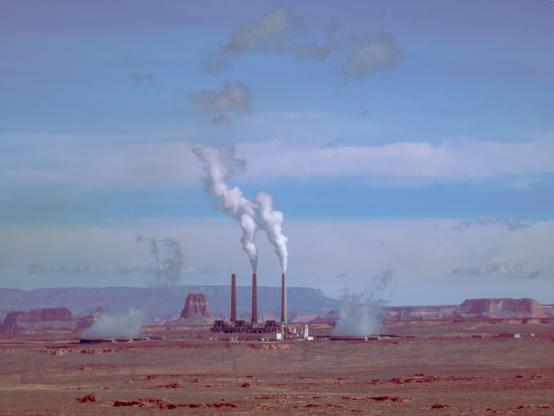 Kraftwerk mit 3 Schornsteinen und Rauchwolken, blauer Himmel, unten rötliche Wüstengegend