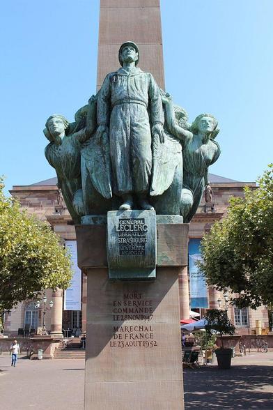 Un grand monument en bronze et pierre, sous un ciel bleu dégagé. Au centre, la statue du Général Leclerc en tenue militaire, debout, le regard levé. Il est entouré de figures allégoriques féminines. L'ensemble est posé sur un haut piédestal en pierre.
Sur le piédestal est inscrit, en relief : "GÉNÉRAL LECLERC LIBÉRATEUR STRASBOURG 23 NOVEMBRE 1944" et plus bas : "MORT EN SERVICE COMMANDÉ LE 28 NOVEMBRE 1947 MARÉCHAL DE FRANCE LE 23 AOÛT 1952"
À l'arrière-plan se trouve un grand bâtiment classique, et de part et d'autre, des arbres. Des personnes sont visibles sur la place.