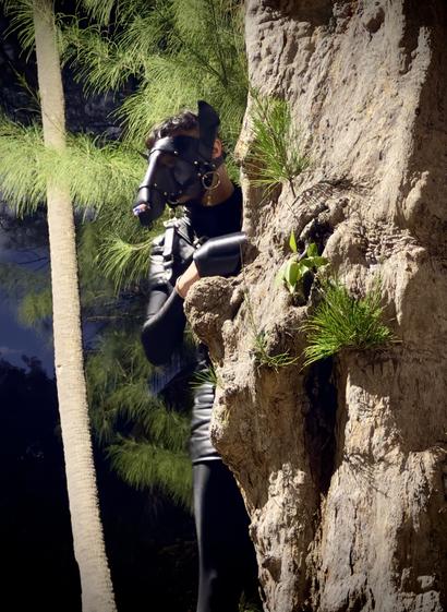 A human horse in black Lycra body suit and leather shirt + shorts peeking from behind a big tree