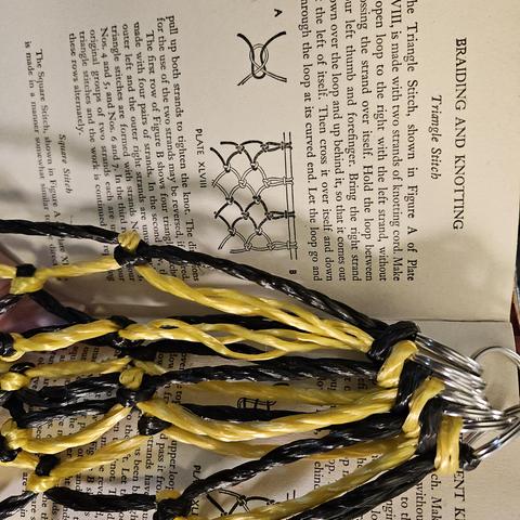 A black and yello poly rope netting. knots tied are shown to be similar to the page behind, which is dracribjng the process and showing the image on how to arrange the thing.