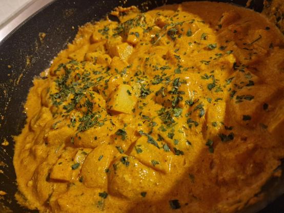 In einer Pfanne ist eine gelb-orangene, cremig aussehende Soße, in welche Kartoffelstücken liegen. Darber idt gehackte Petersilie gestreut