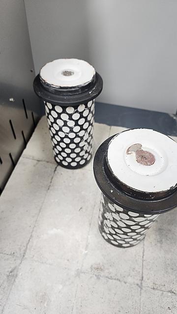 Two large casting flasks cool on a firebrick pad. The one on the left has been cooling longer which you can see by the silver color. The one on the right still has a pink glow. 
~
Twee grote gietkruiken koelen af op een vuurstenen plaat. Die aan de linkerkant koelt al langer af, wat je kunt zien aan de zilveren kleur. Die aan de rechterkant heeft nog een roze gloed.
~
Deux grands cylindres de moulage refroidissent sur une plaque en brique réfractaire. Celui de gauche refroidit depuis plus longtemps, ce que l’on voit à sa couleur argentée. Celui de droite a encore une lueur rosée.