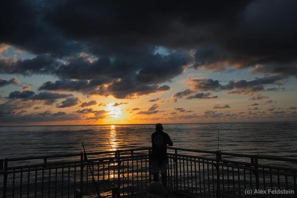 Sunrise at the fishing pier with a fisherman silhouette in front