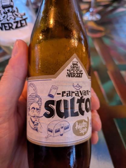 A bottle of beer with a black and white logo which says Caravan Sultan, which os beimg held in a hand.