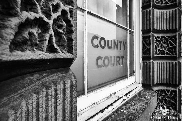 Monochromatic low-angle shot of a window reading "County Court". Ornate stone details frame the window, showcasing the historic architecture.