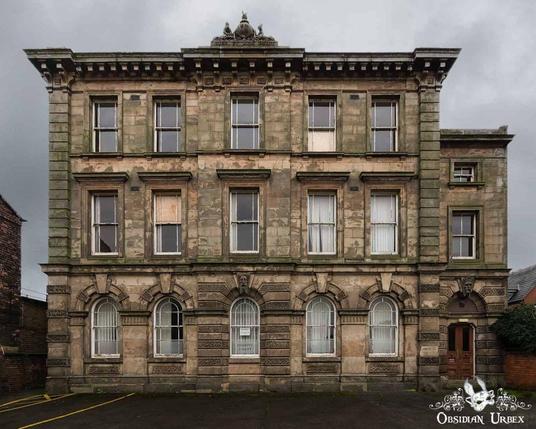 A stately stone courthouse with symmetrical window arrangements stands under a cloudy sky. The historic building, detailed with arches and cornices,