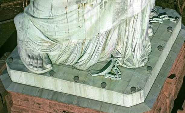 Photograph of the base of the Statue of Liberty. Seen are her right foot, some broken shackles and chains. and near her left foot, more broken chains.