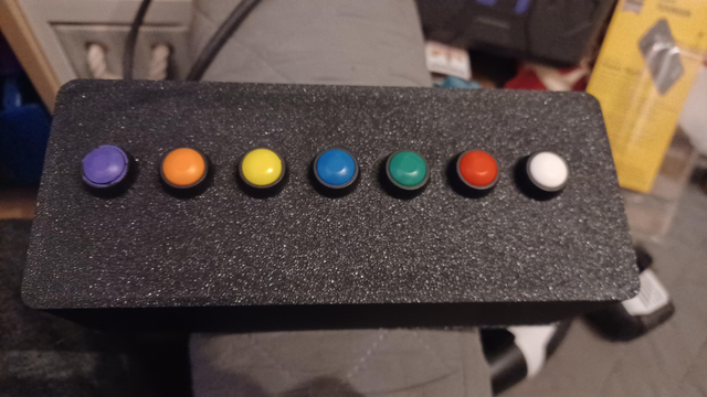 Picture of top of box with 7 coloured buttons (white, red, green, blue, yellow, orange and purplle)