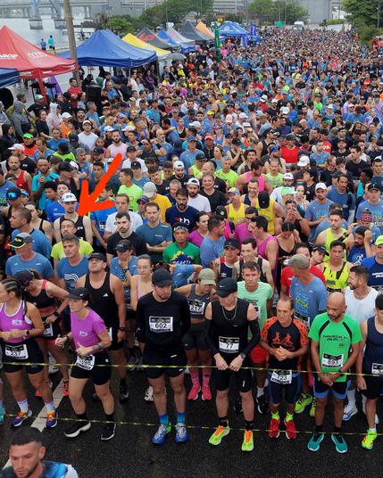Multidão de competidores das provas de 21 km e 15 km concentrados na largada. Autor indicado por uma flecha.