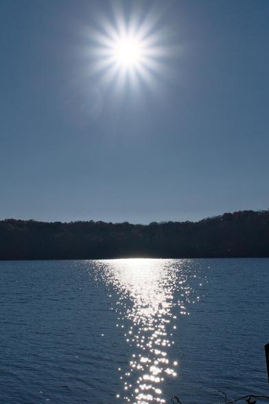 A bright diamond morning sun high in the blue sky over a lake which reflects the sunlight in ripples