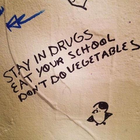 graffiti that says stay in drugs, eat your school, don't do vegetables. there's a cute drawing of a penguin underneath.