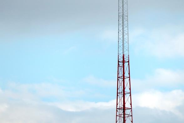 part of a red and white radio antenna tower against a sky lightly brushed with white and gray clouds