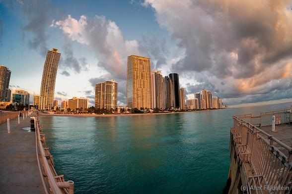 Sunny Isles Beach with a fisheye showing pier, buildings, ocean, and sky with clouds.