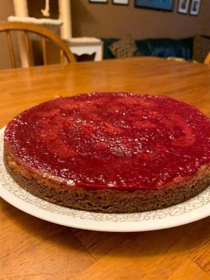 A vegan cheesecake with red topping on a white plate on a wooden table.